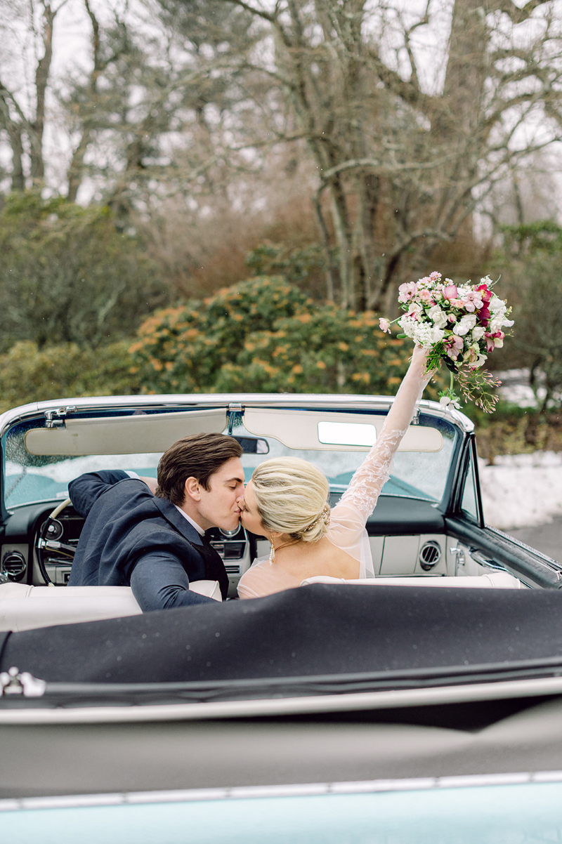 Bride and Groom drive away from their wedding venue in a vintage getaway car